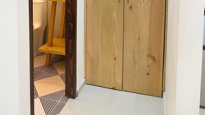 Un armario de madera con dos puertas, un taburete de madera pequeño y un lavabo negro sobre un suelo de baldosas blancas.
