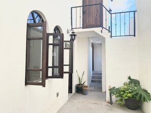 A narrow, white-walled corridor with a wooden door and a small balcony with a metal railing.