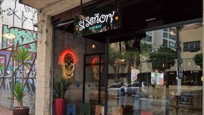 Ein Schaufenster mit einem Neon-Schild mit der Aufschrift "Si Senor!" und einer großen Glasfront, die die Straße reflektiert.