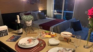 Ein liebevoll gedeckter Esstisch mit Tellern, Besteck und einer Champagnerflasche, ein Bett mit Ausblick und ein Schild mit der Aufschrift 'HOME WHERE THE LOVE IS'.