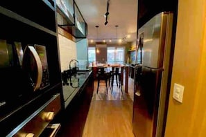 Uma cozinha moderna com eletrodomésticos de aço inoxidável, piso de madeira e um espaço de refeições com banquetas.
