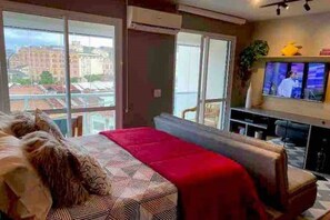 A modern living room with a large bed, a TV, and a view of buildings outside. - Modern Loft Style (São Paulo)