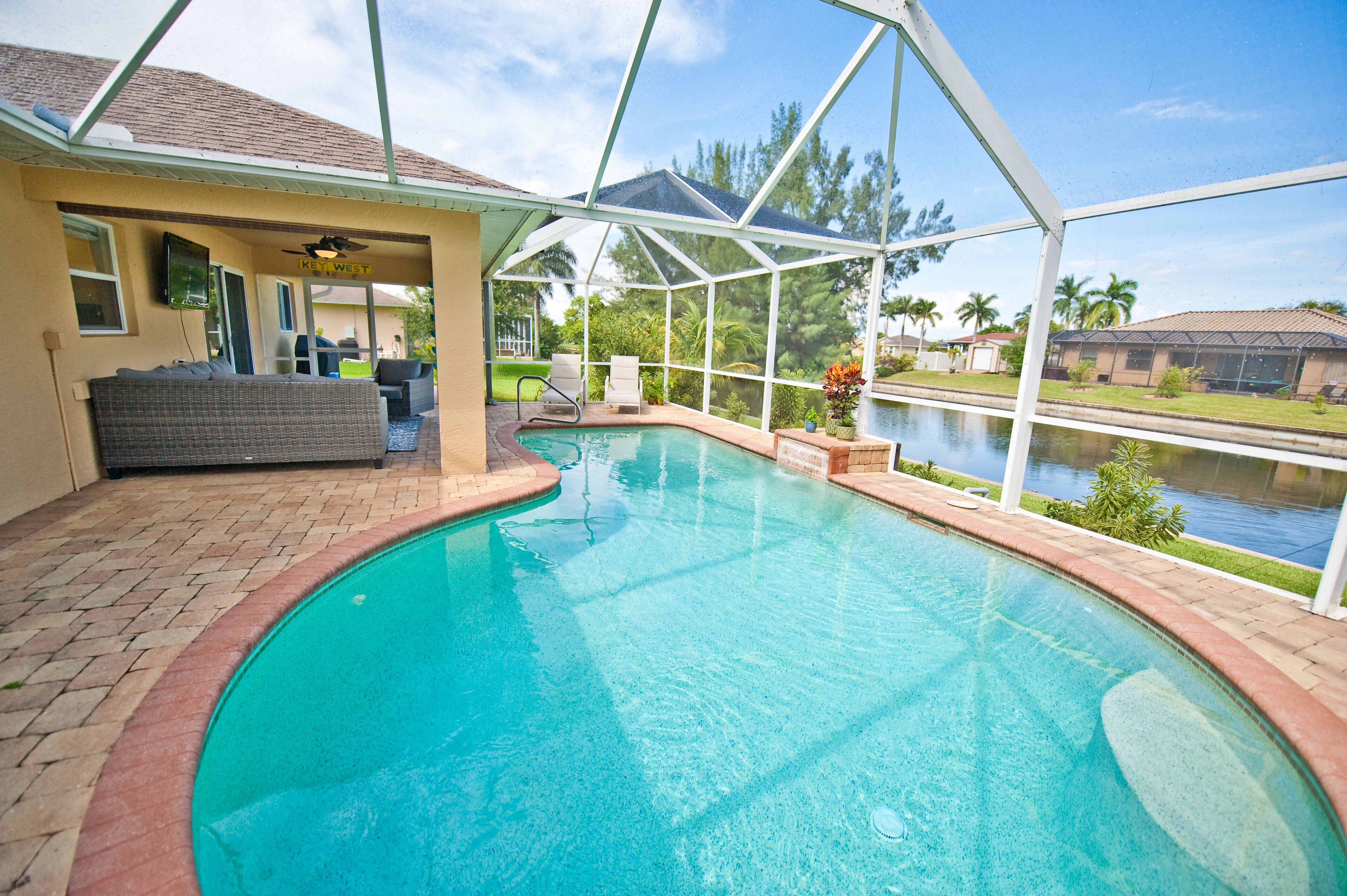 A swimming pool with a covered patio area, a ceiling fan, and a view of a body of water.