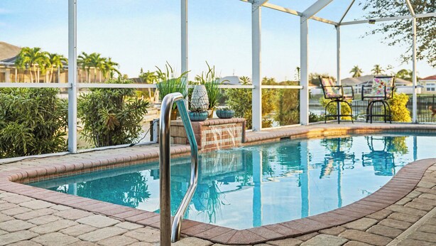A swimming pool with a glass enclosure, surrounded by potted plants and lounge chairs. - Flamingo's Nest - A Tropical Waterfront Pool Oasis (Cape Coral)