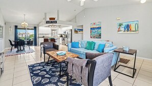 A spacious living area with a blue sofa, a wooden coffee table, and a dining area with a chandelier. - Flamingo's Nest - A Tropical Waterfront Pool Oasis (Cape Coral)