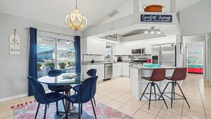 A modern kitchen with white cabinets, stainless steel appliances, and a central island with bar stools. - Flamingo's Nest - A Tropical Waterfront Pool Oasis (Cape Coral)