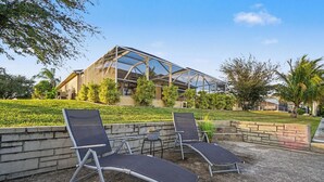 A modern building with a glass facade, a patio area with two lounge chairs, and a well-maintained lawn. - Flamingo's Nest - A Tropical Waterfront Pool Oasis (Cape Coral)