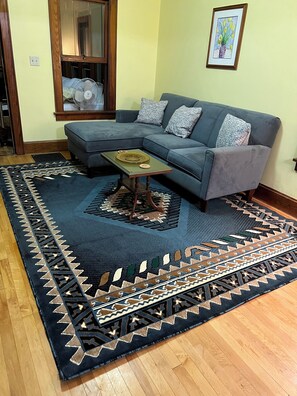 A living room with a sectional sofa, a coffee table, a patterned rug, and a framed picture on the wall.