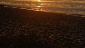 Un atardecer sobre una playa con agua tranquila que refleja el sol.