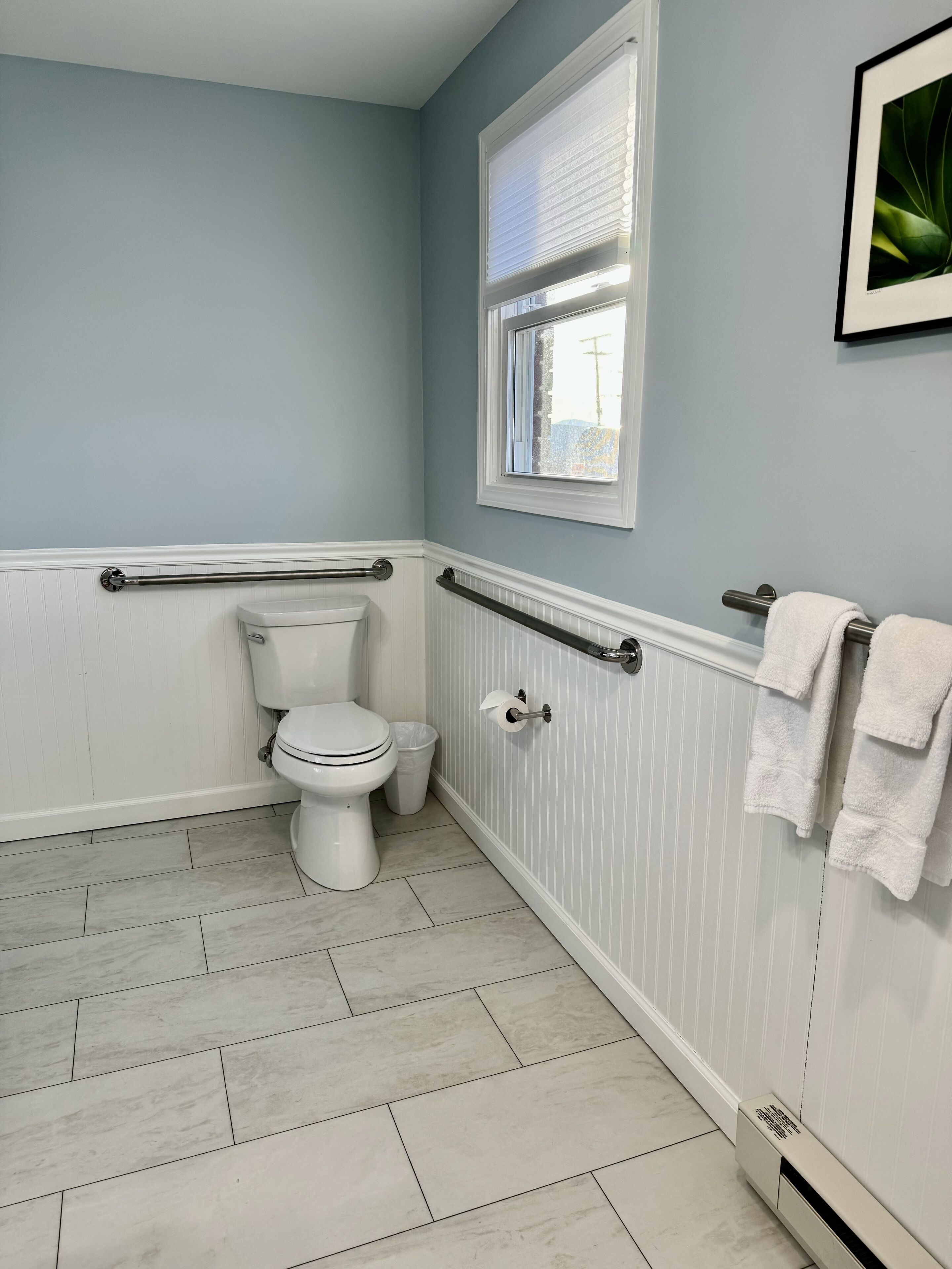 A bathroom with a toilet, a window, a towel rack, and a radiator.