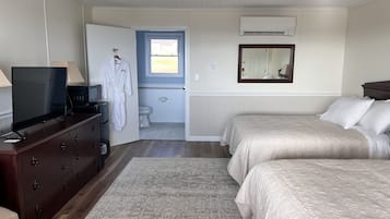 A bedroom with a TV on a dresser, a bathroom with a toilet and sink, and two beds with beige bedding.