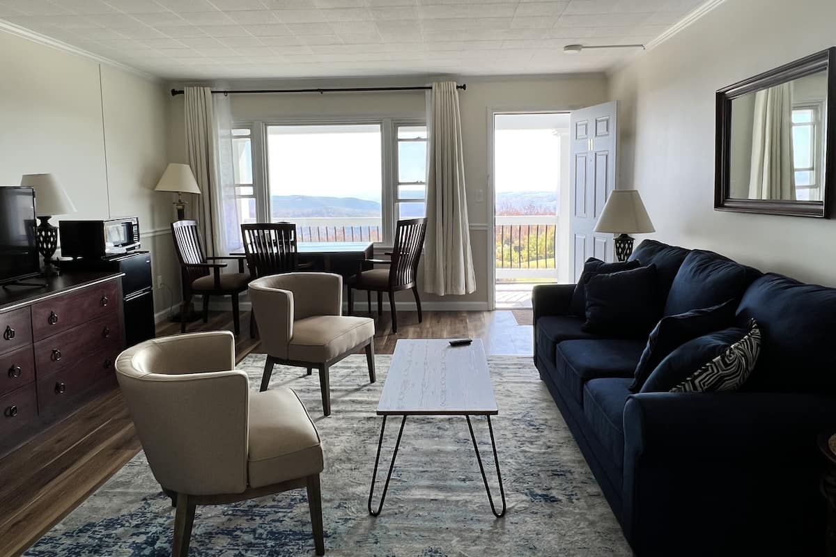A living room with a sofa, chairs, a coffee table, a TV, and a view through large windows.