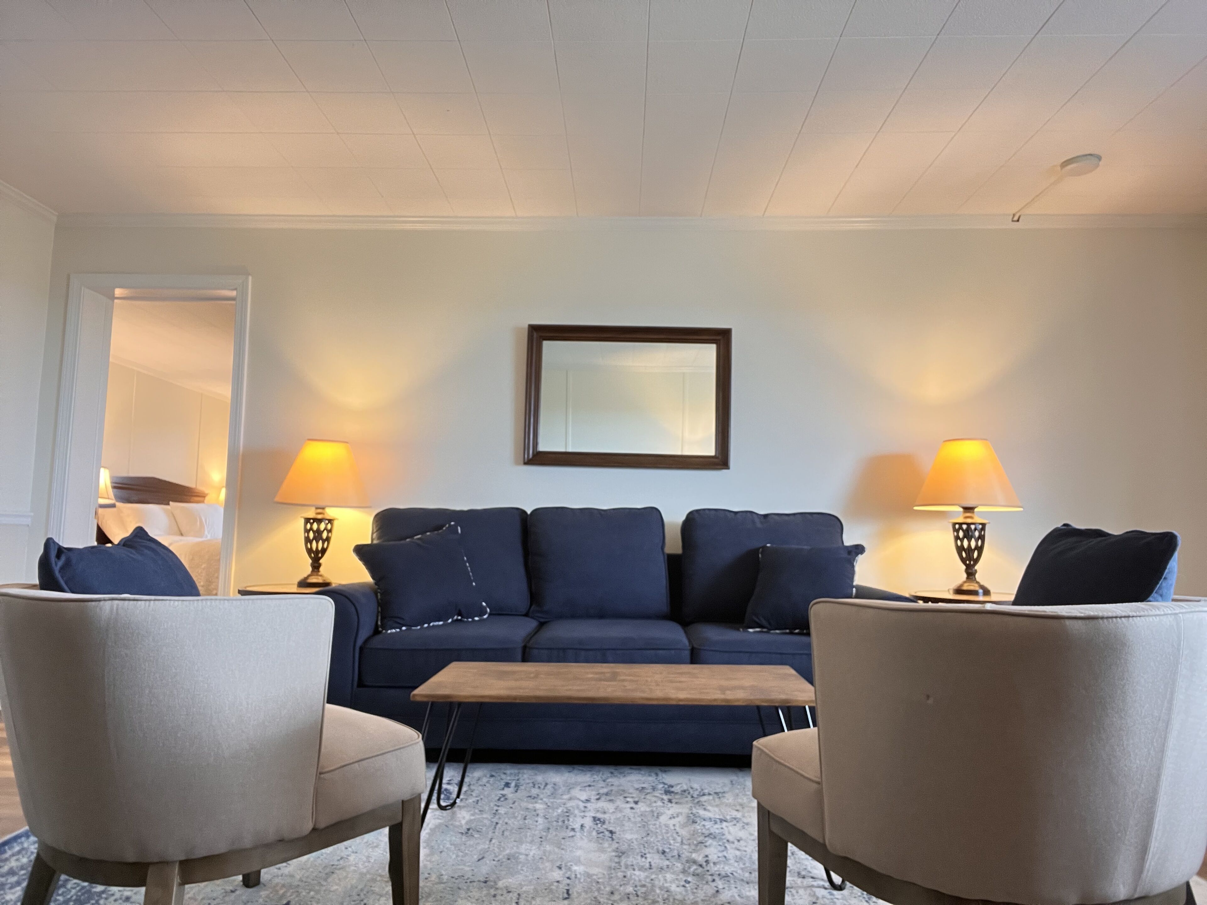 A living room with a dark blue sofa, two armchairs, a coffee table, and two lamps.