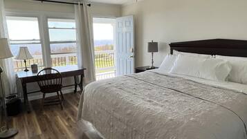 A hotel room with a large bed, a desk, and a chair. There are windows with a view of the outdoors.