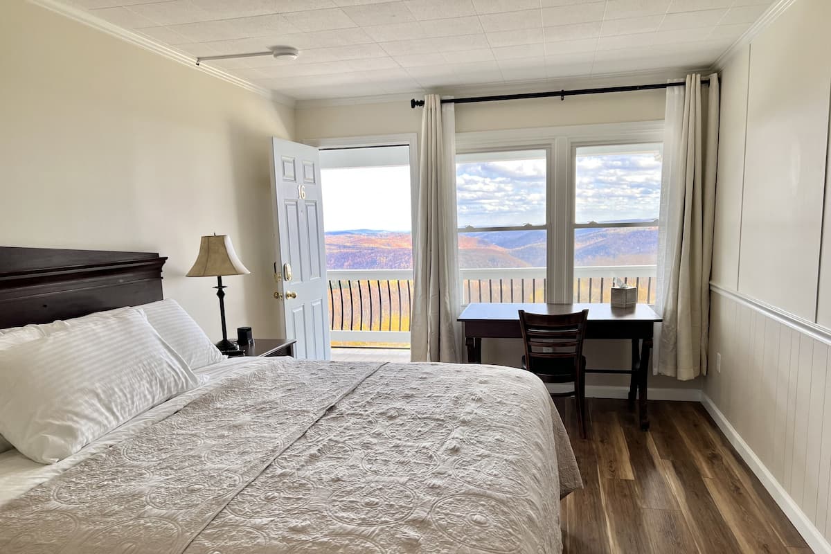 A bedroom with a large bed, a desk, and a view of the mountains through a window.