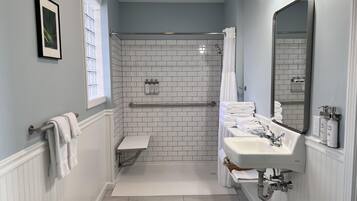 A bathroom with a white tiled shower, a sink with a mirror, and a towel rack.