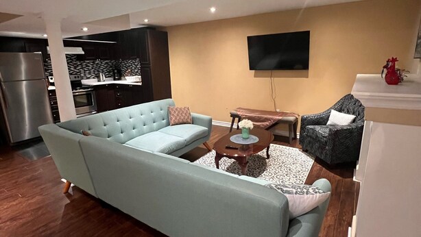 A modern living room with a light blue sofa, a coffee table, and a television mounted on the wall. - Bright and Clean Basement Apartment,5 min to Lakes. (Richmond Hill)