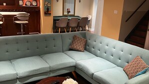 A living room with a light blue sectional sofa, a wooden coffee table with a vase of white flowers, and a patterned rug. - Bright and Clean Basement Apartment,5 min to Lakes. (Richmond Hill)