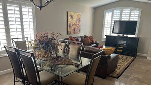 A dining area with a glass table and chairs, a sofa, a TV, and a painting on the wall. - Desert Ridge * Location Location Location  (Phoenix)
