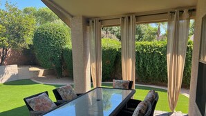 An outdoor patio with a glass-top table surrounded by wicker chairs with floral cushions, set against a backdrop of greenery and a clear sky. - Desert Ridge * Location Location Location  (Phoenix)