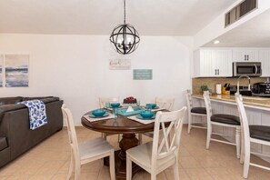 Comedor con mesa redonda, sillas y candelabro. Zona de cocina con armarios blancos y microondas.