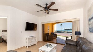 Una sala moderna con un sofá, una mesa de centro y un televisor. Cuenta con un balcón con vista a la playa y palmeras.