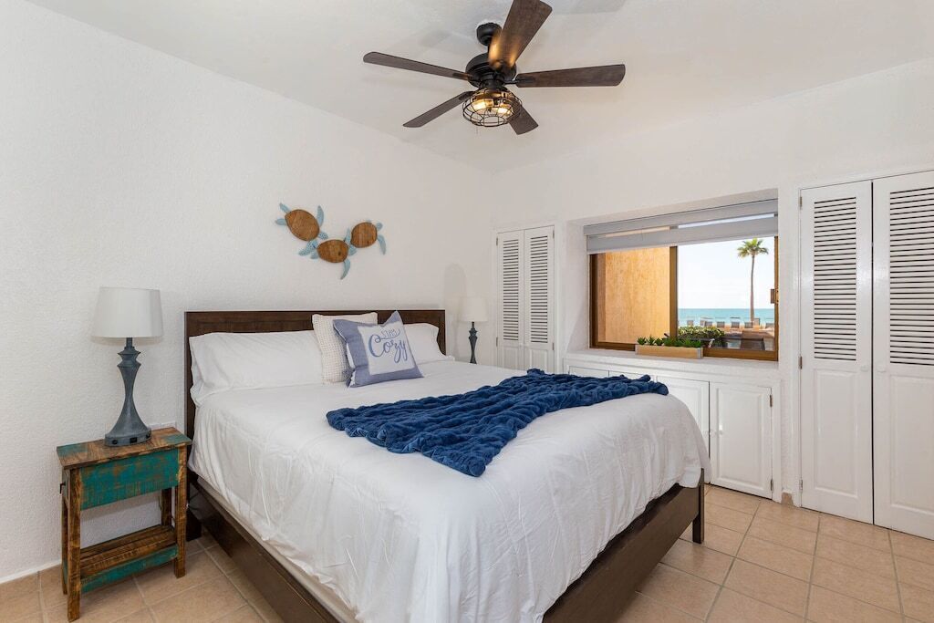 Ein Schlafzimmer mit Bett, Deckenventilator, Nachttisch, Fenster mit Rollläden und Meerblick.