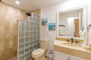 Un baño con cabina de ducha de vidrio, inodoro, lavabo con espejo y toallero.