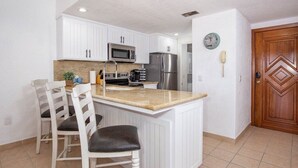 Cocina con armarios blancos, encimera de granito, refrigerador de acero inoxidable y puerta de madera.