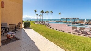 Un área de piscina con varias piscinas, palmeras y un patio con sillas y una mesa.