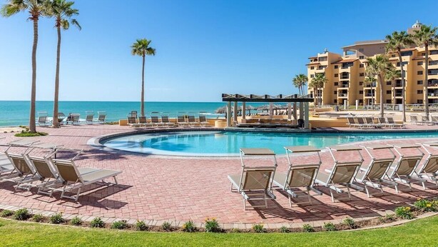 Zona de piscina en un resort con sillones de descanso, una cabaña y vista al océano.