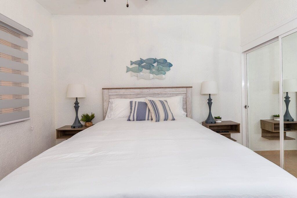 A bedroom with a large bed, two bedside tables with lamps, a wall-mounted fish decoration, and a sliding glass door.