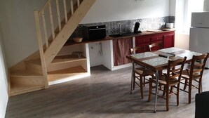 Una cocina con una escalera de madera, una mesa de comedor con sillas y un refrigerador.
