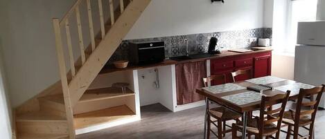 Una cocina con una escalera de madera, una mesa de comedor con sillas y un refrigerador.