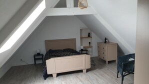 Un dormitorio con techo inclinado, una cama, un aparador, una silla y una mesita.