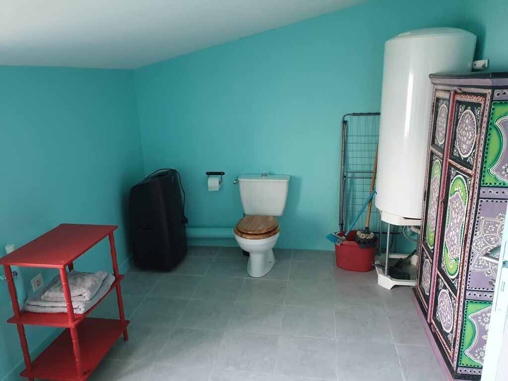 Une petite salle de bain avec des toilettes, une étagère rouge, un sac noir et un chauffe-eau.