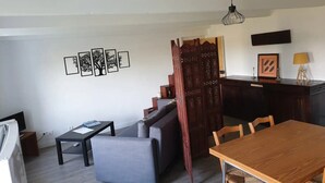 Una sala de estar moderna con un sofá, una mesa de comedor y una zona de cocina con un armario de madera y un televisor.