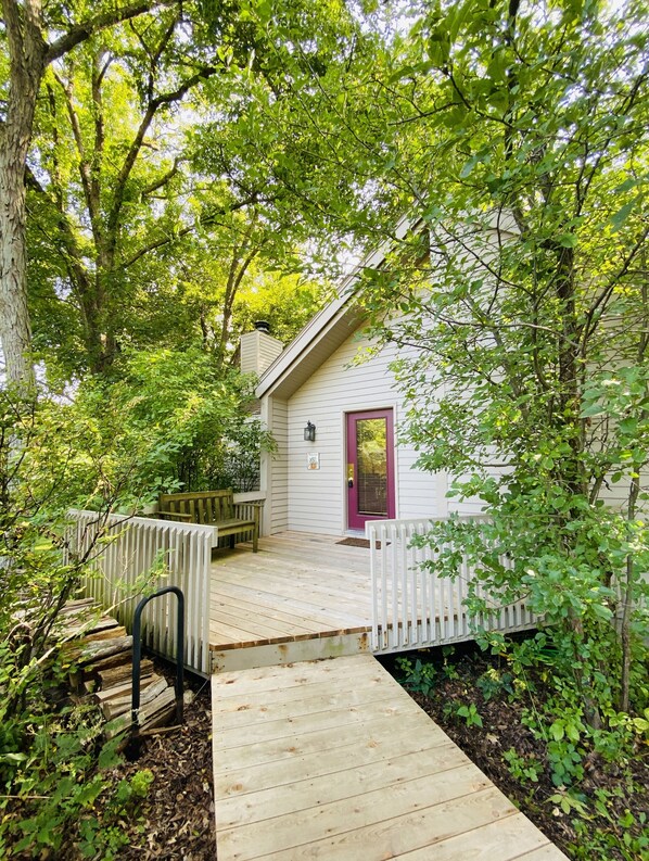 A wooden deck leading to a white building with a purple door, surrounded by lush greenery. - Private 3BR/2BA near golf, historic Galena, lake, owner's club, hiking, skiing (Galena)