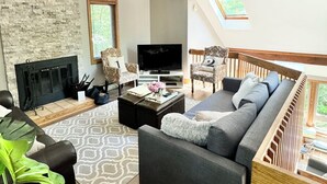 Een ruime woonkamer met een open haard, een bank, een televisie en een dakraam.