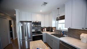 A modern kitchen with stainless steel appliances, a wooden dining table, and a window providing natural light. - Beautiful 3-bedroom home on the Canal with patio. (Galveston)