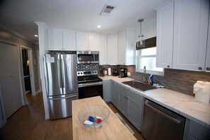 A modern kitchen with stainless steel appliances, a wooden dining table, and a window providing natural light. - Beautiful 3-bedroom home on the Canal with patio. (Galveston)