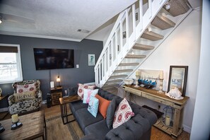 A living room with a grey sofa, patterned armchair, and a staircase with woven steps.