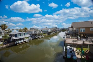 A canal with boats docked on wooden piers, surrounded by residential buildings and palm trees. - Beautiful 3-bedroom home on the Canal with patio. (Galveston)