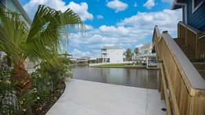 A waterfront property with a wooden deck, a concrete pathway, and a view of the water. - Beautiful 3-bedroom home on the Canal with patio. (Galveston)