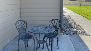 Un patio con una mesa y sillas, piso de concreto y vista a una casa y montañas al fondo.
