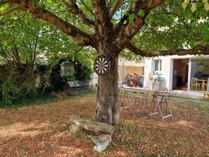 Relax in a serene garden setting surrounded by lush greenery and a tranquil tree, perfect for outdoor dining or relaxation.