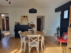 Relax in this stylish living area with a round dining table, black pendant light, and a grand piano.