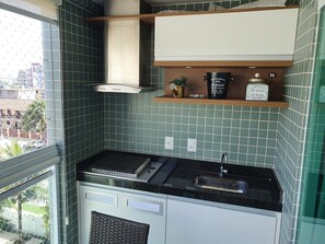 Una cocina compacta con estufa a gas, lavamanos y horno integrado. Se aprecia una ventana con vistas a edificios.