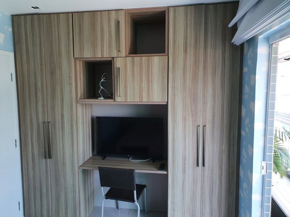 Quarto com escrivaninha embutida, cadeira e televisão.