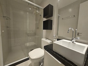 Un baño moderno con ducha de vidrio, inodoro blanco, lavabo con espejo y encimeras negras.